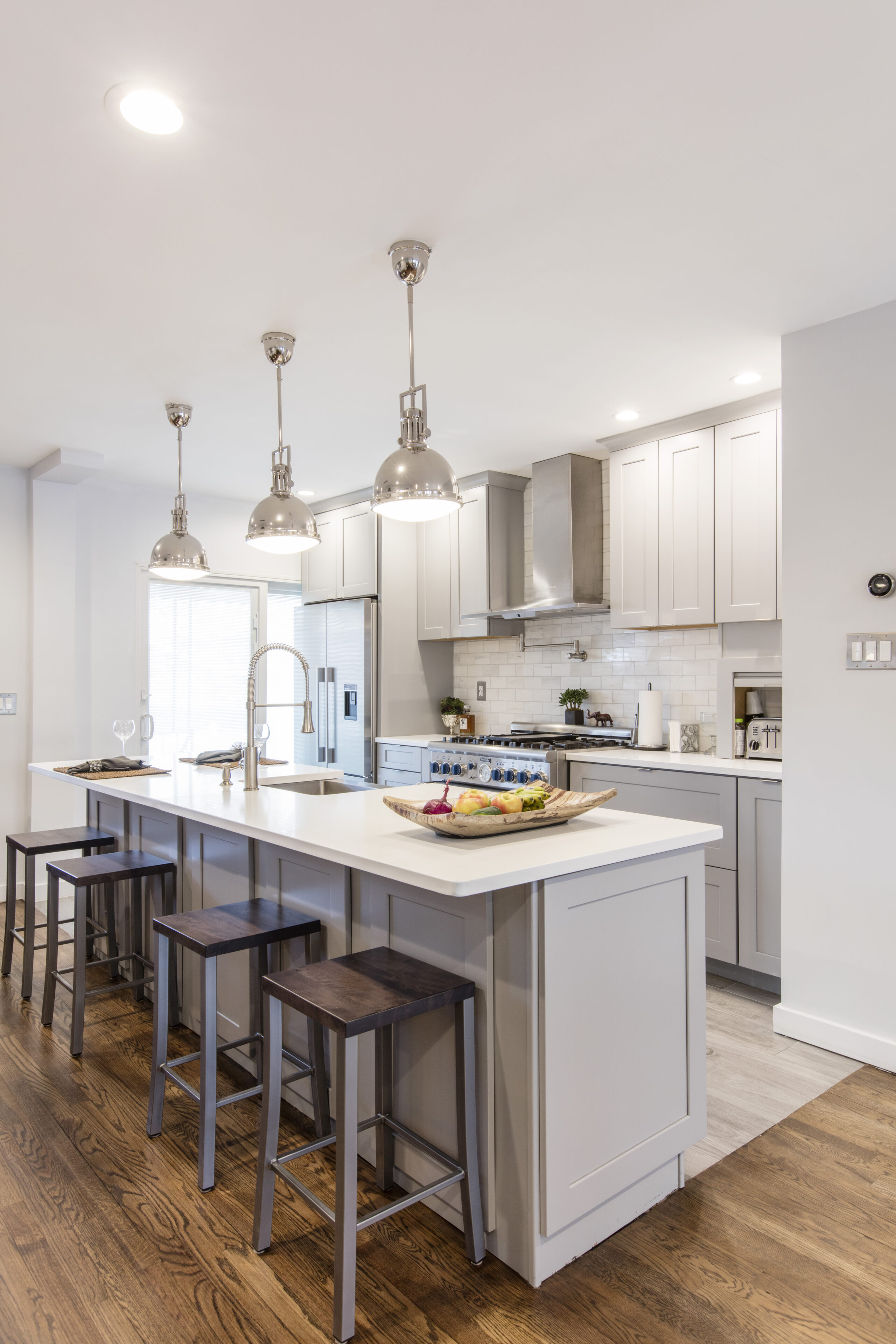 A well-lit kitchen with gray cabinets, stainless steel appliances, and a clean, organized countertop space with a wooden floor.