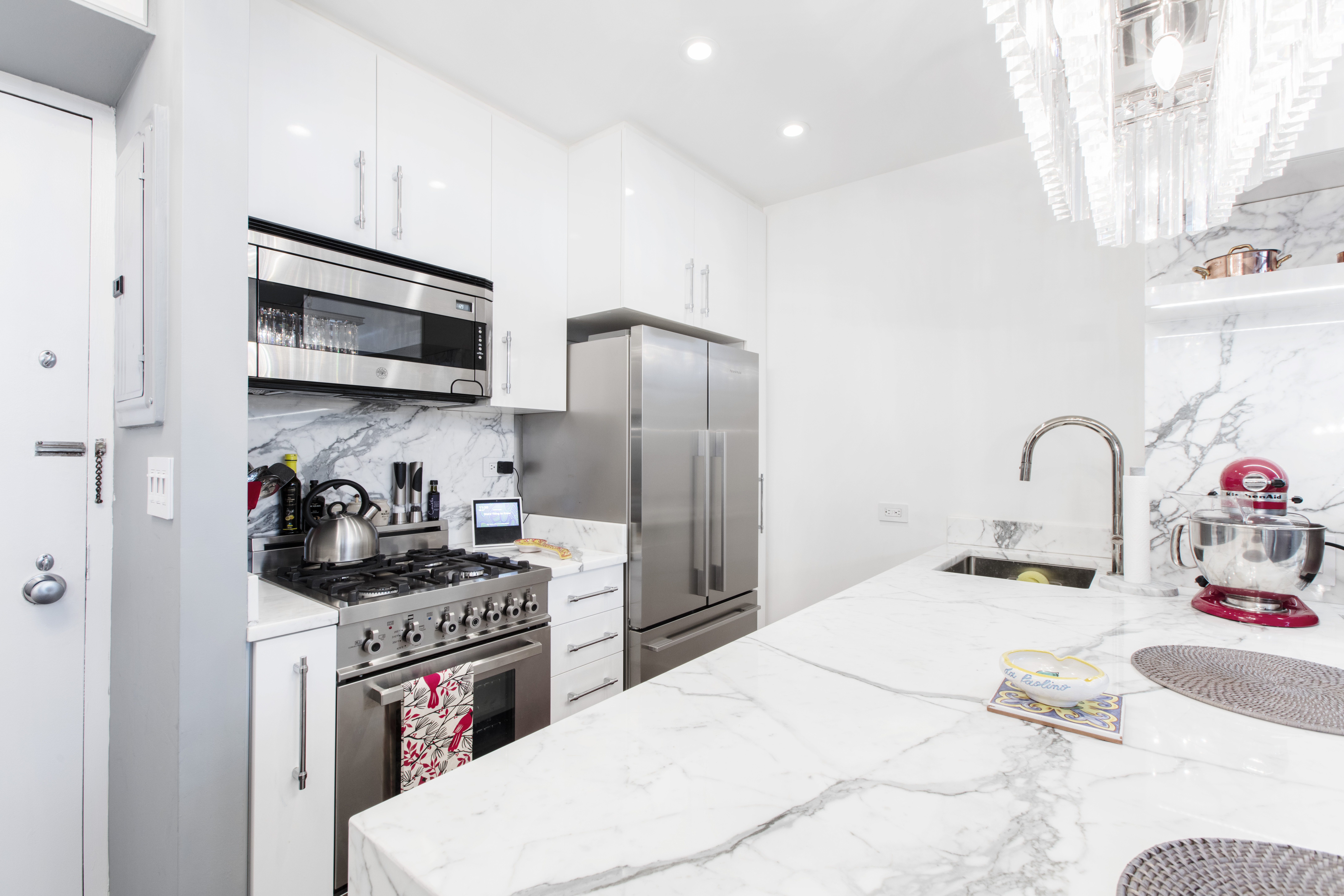 Calacatta marble kitchen peninsula with white cabinetry, strove, and refrigerator