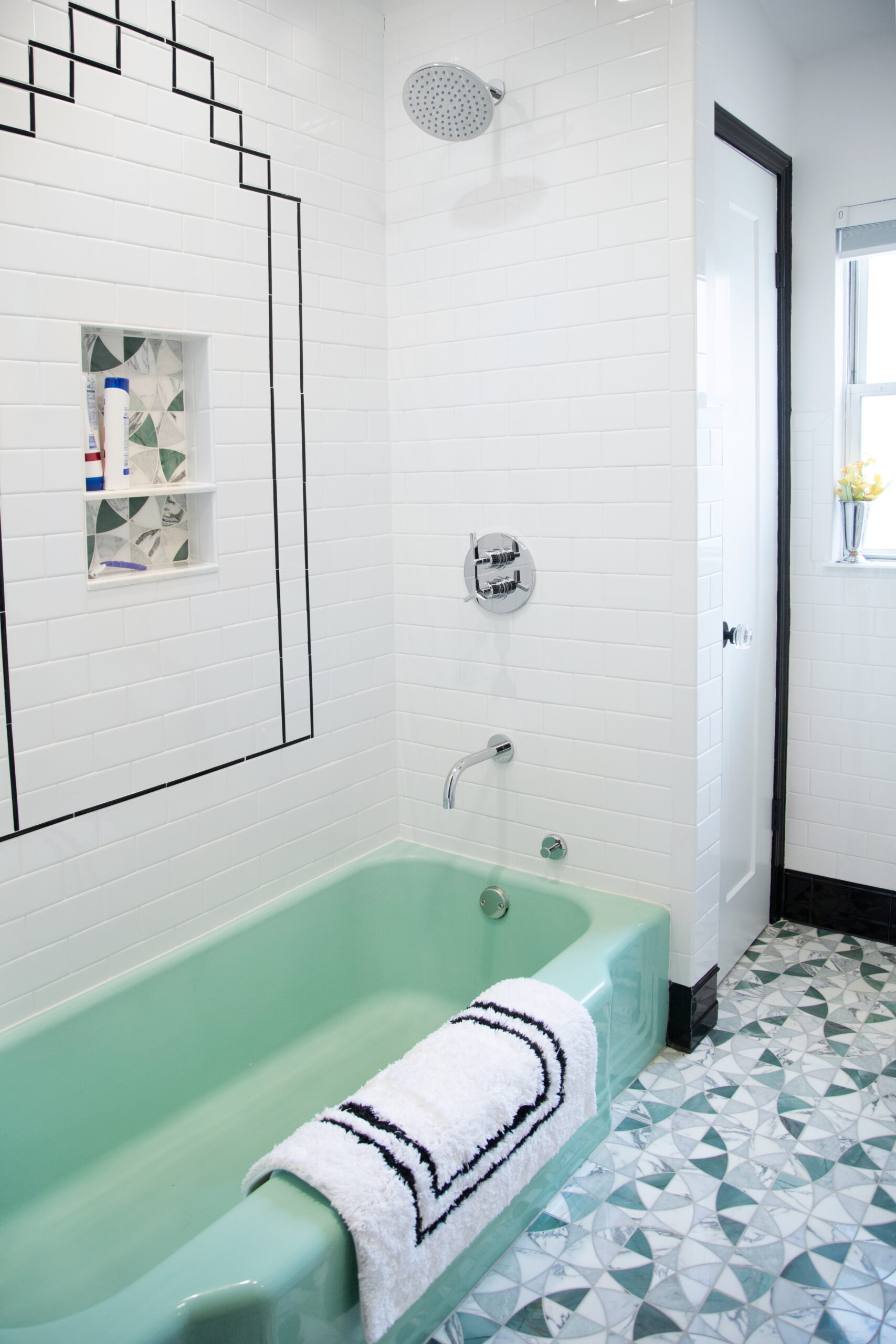 Mint green bathtub with black pencil border and mosaic-lined niche, set in white subway tile, Jersey City bathroom remodel.