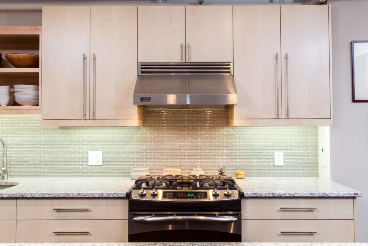 beige kitchen cabinets and marble countertop and pastel green backsplash tiles and stainless steel gas cooking range with hood after renovation