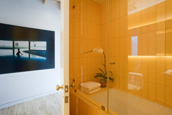 bright yellow tiles on bathroom walls and white bathtub with glass door after renovation