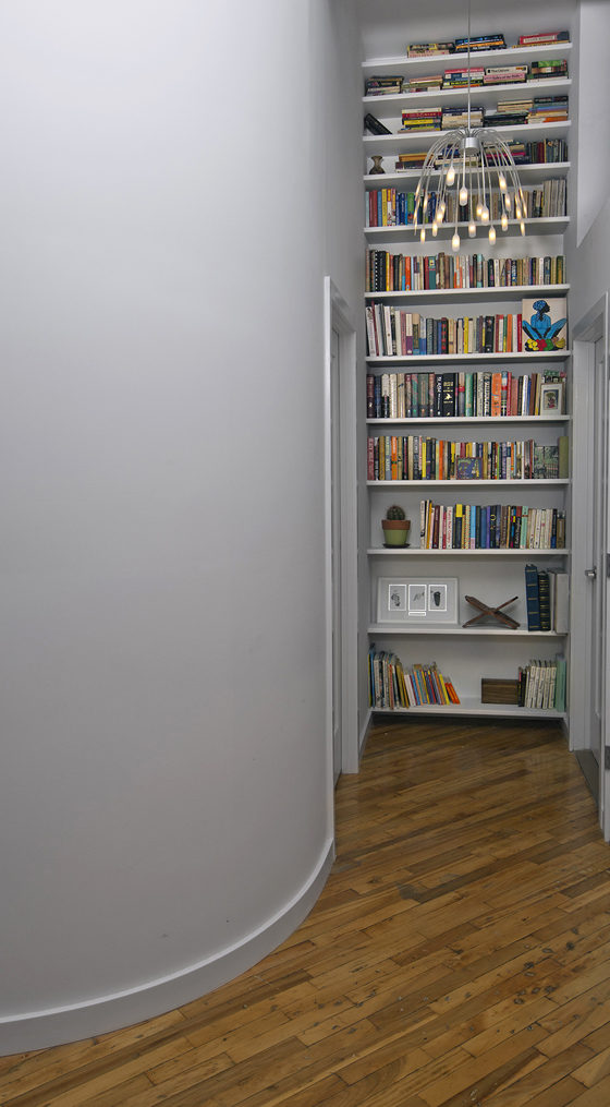 built-in floor to ceiling book shelves at the end of hallway with hardwood floors and pendant light and gray walls after renovation