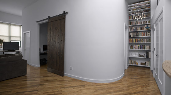 living room and hallway with hardwood floors and gray walls and barn door and round wall corner floor to ceiling built-in bookshelves at the end of hallway after renovation