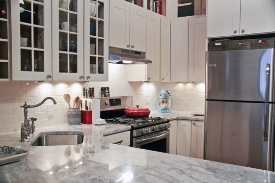 white kitchen cabinets with gray marble countertop and stainless steel undermount sink with see through overhead cabinets and under cabinet lighting and stainless steel appliances after renovation