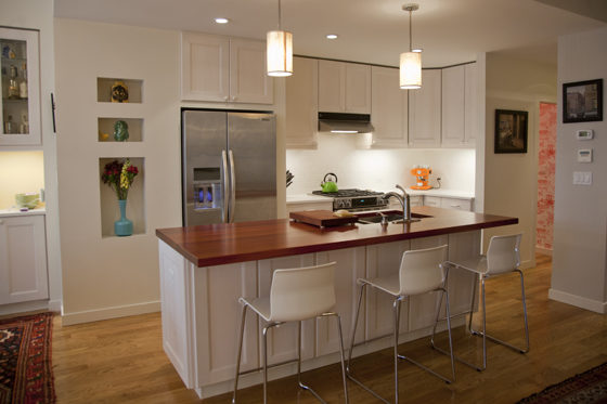 island with butcher block countertop and pendant lights and white kitchen cabinets after renovation