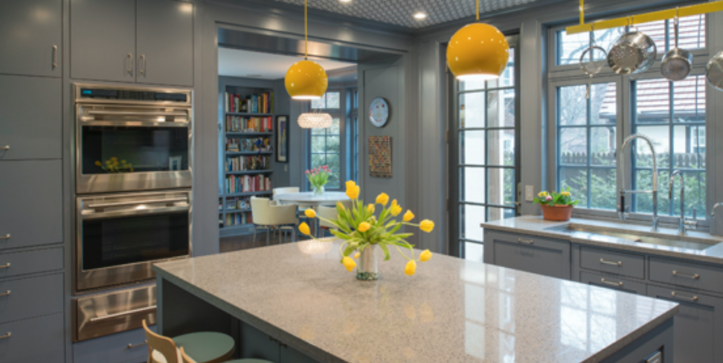 gray kitchen cabinets with stainless steel appliances and island with marble countertop and yellow pemdant lights after renovation