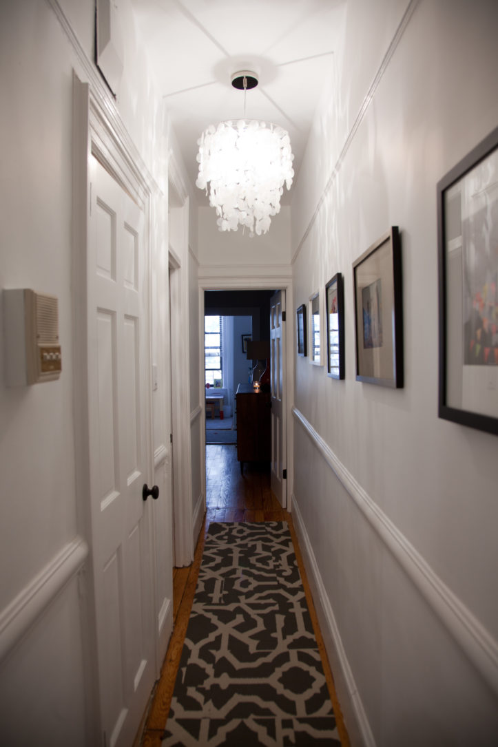 hallway with white walls and chair rails and hardwood floors and chandelier after renovation