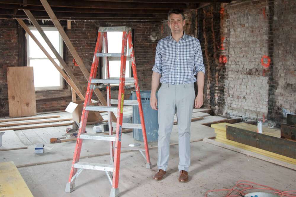 man standing near a ladder in a room with brick walls during renovation