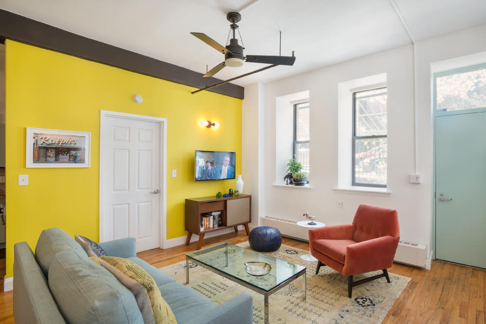 living area with hardwood floors and fan and accent yellow wall after renovation