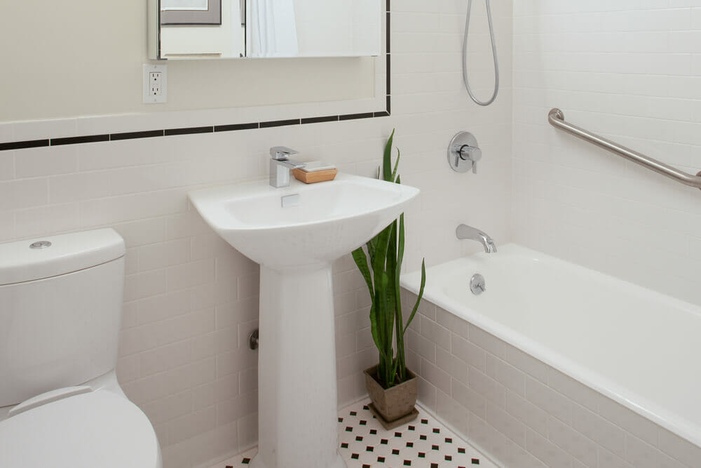 small full bathroom with white wall tiles and pedastal sink with mirrored medicine cabinets and white and black floor tiles and toilet after renovation