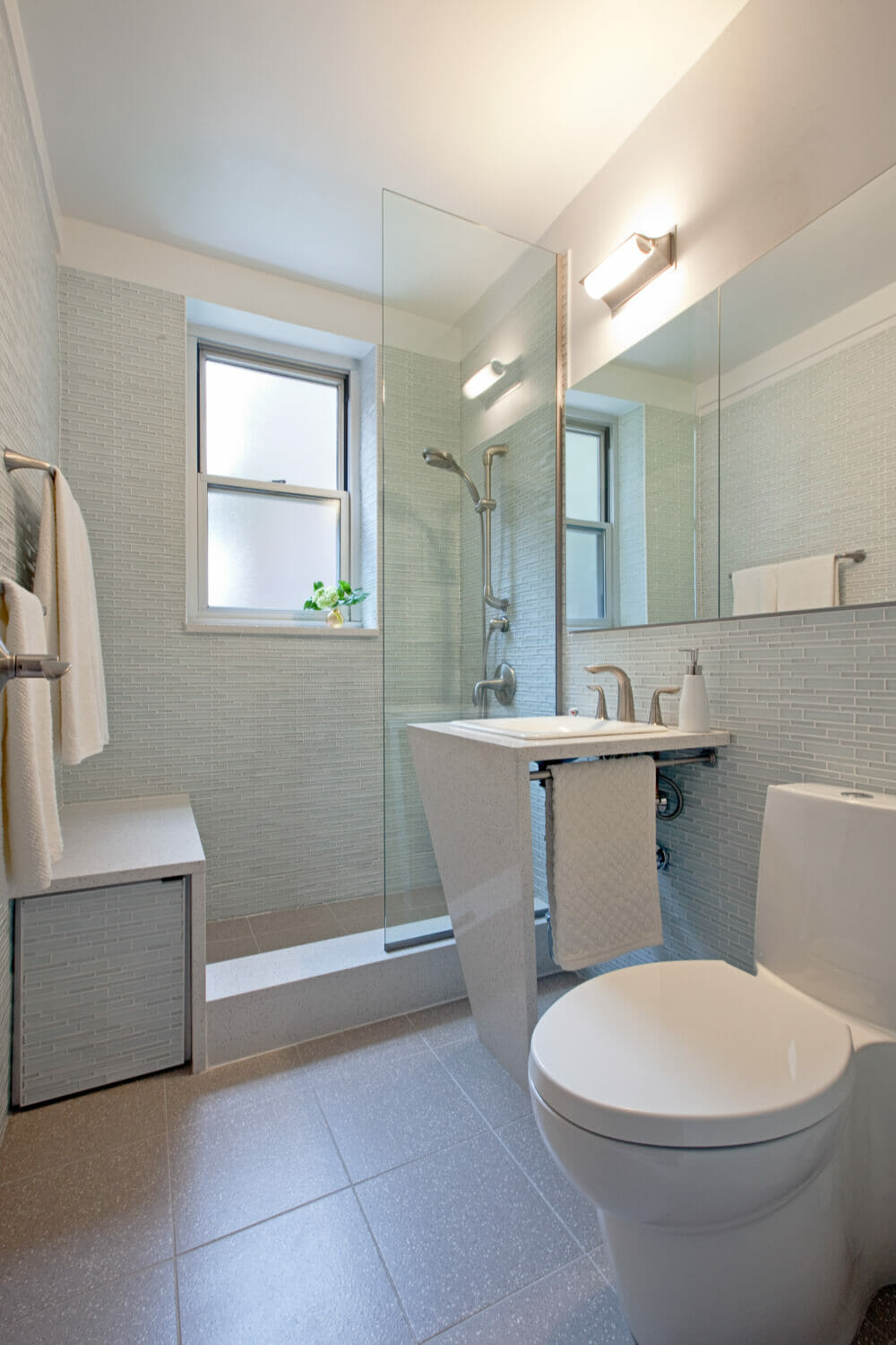bathroom with contemporary pedastal sink and toilet and walk-in shower with half glass wall and beige floor tiles after renovation