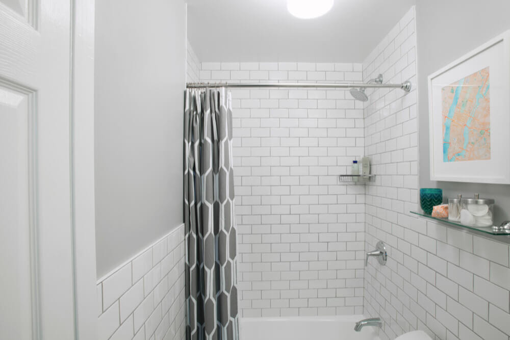 bathroom with white subway wall tiles and gray wall paint and a glass shelf below medicine cabinet after renovation