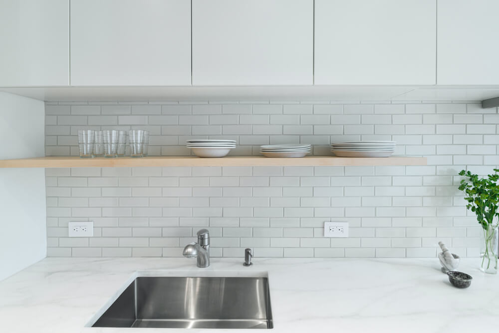 white subway tiled backspash in a white kitchen with white countertop and steel sink and closed white kitchen cabinets after renovation 