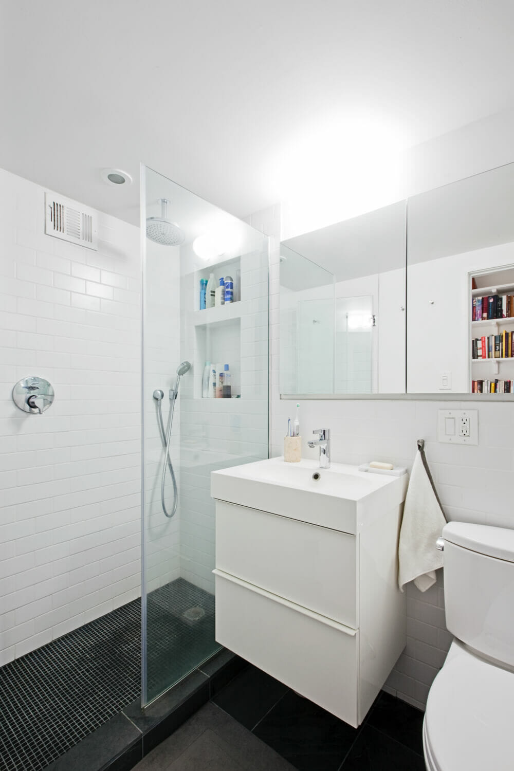 white bathroom with black floor tiles and floating vanity and mirror and walk in shower with subway tiles on wall after renovation