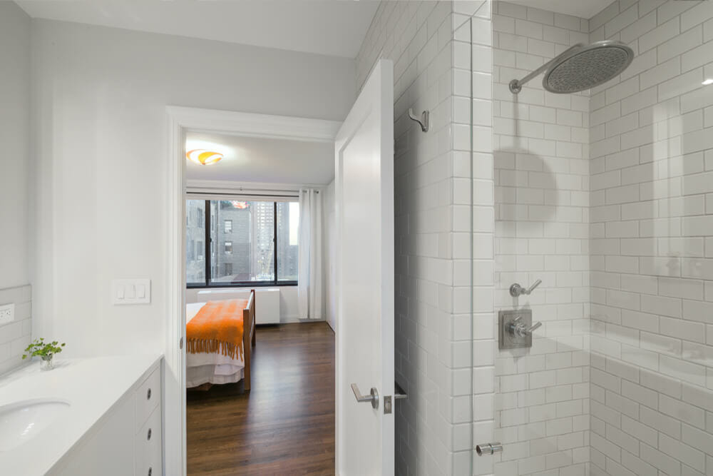 walk-in shower with glass door and white subway tiles on walls and door that opens to bedroom with hardwood floors after renovation