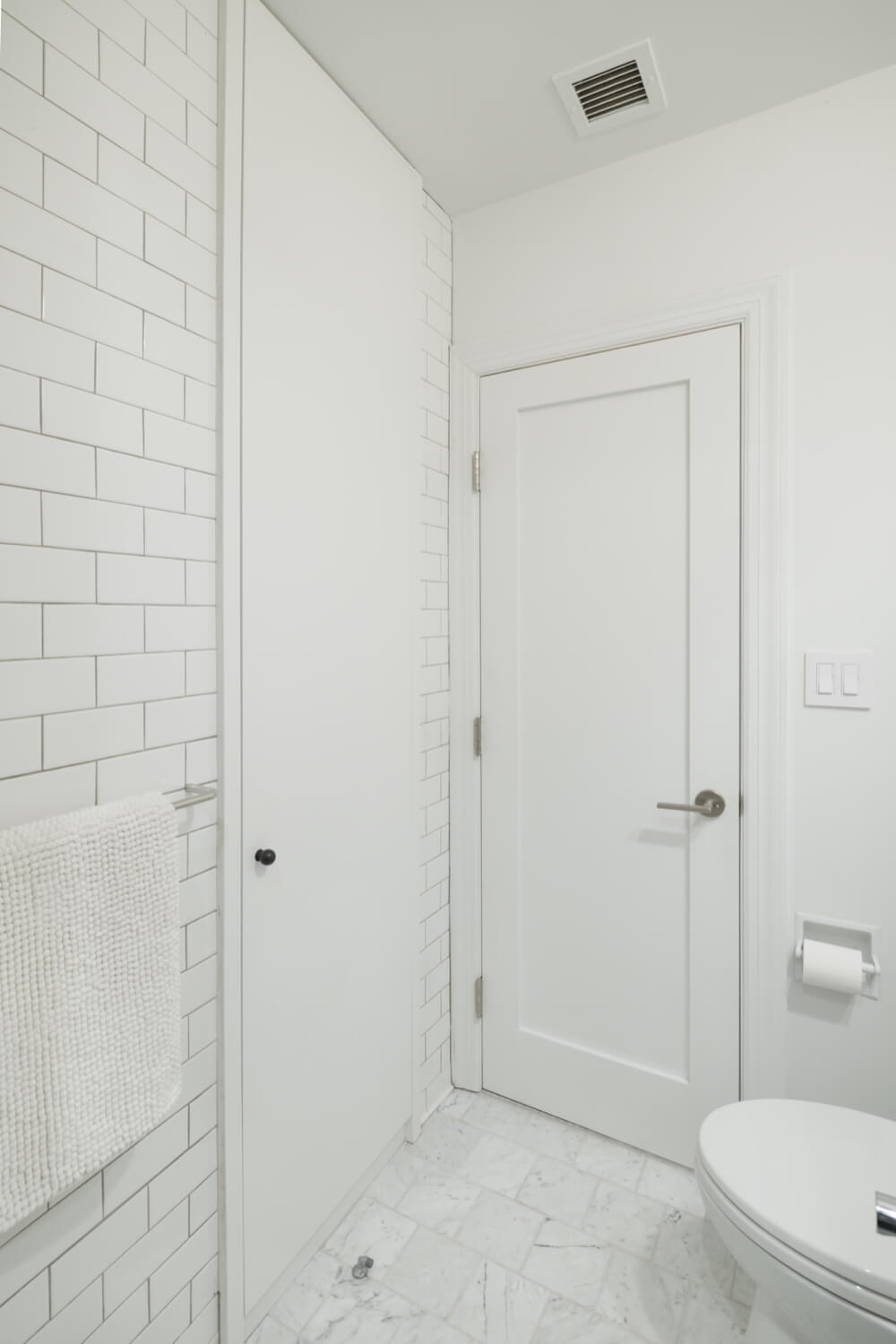 all white bathroom with subway tiles on walls and white flooring and toilet after renovation