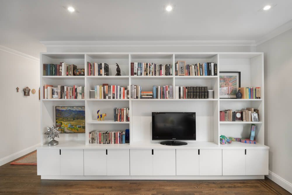 large built-in entertainment unit with book shelves and storage cabinets in living room with recessed lighting and hardwood floors after renovation