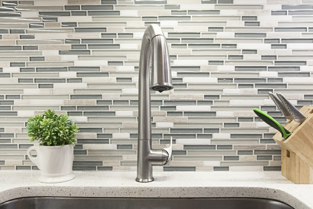 white countertop with undermount sink and nickel pull out faucet and glass mosaic tile backsplash after renovation