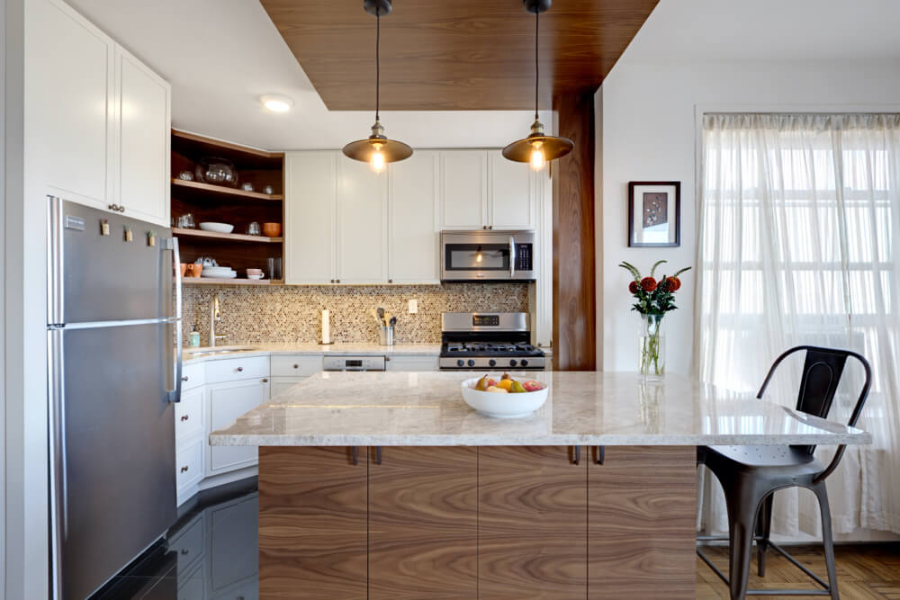 small kitchen with white cabinets and stainless steel appliances and natural wood island with marble countertop and pendant lights after renovation