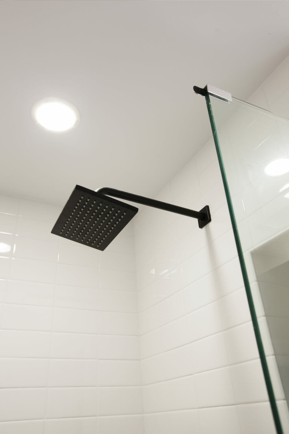 shower with half glass wall and recessed lights and subway tiles on wall and black square rainfall shower head after renovation