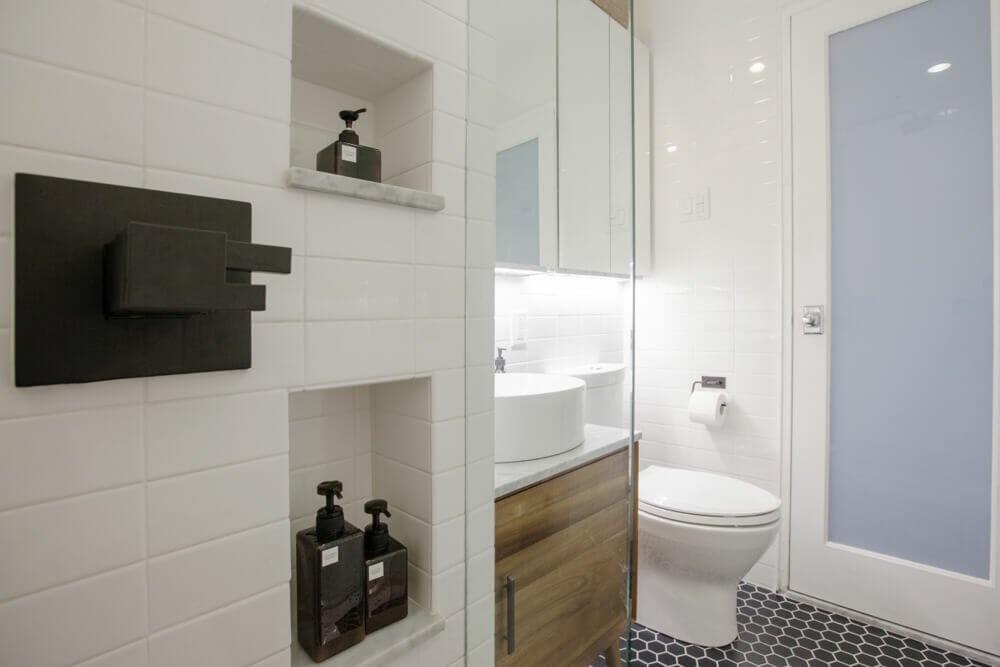 shower with recessed shelves and white subway tiles and matte black shower thermostatic fixtures and black hexagon floor tiles and natural wood vanity with vessel basin sink after renovation