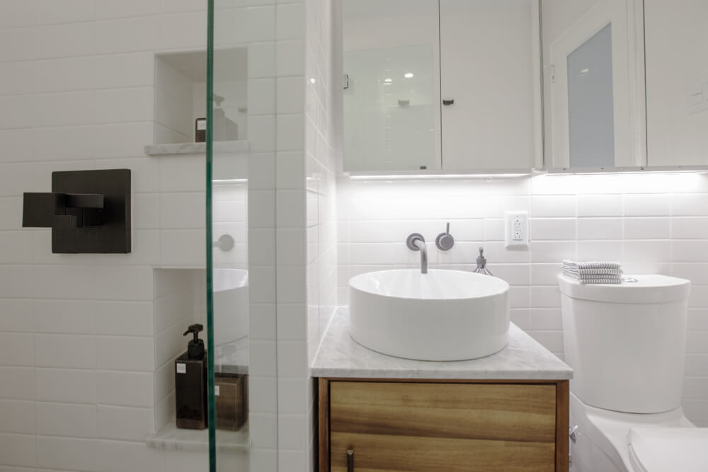 walk-in shower with recessed shelves and half glass wall and vanity with round vessel sink and mirrored medicine cabinet and contemporary toilet after renovation