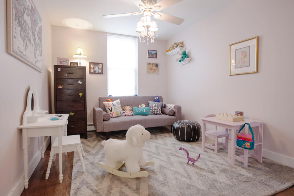 kids playroom with window and soft pink wall paint and hardwood floors and ceiling fan with chandelier after renovation