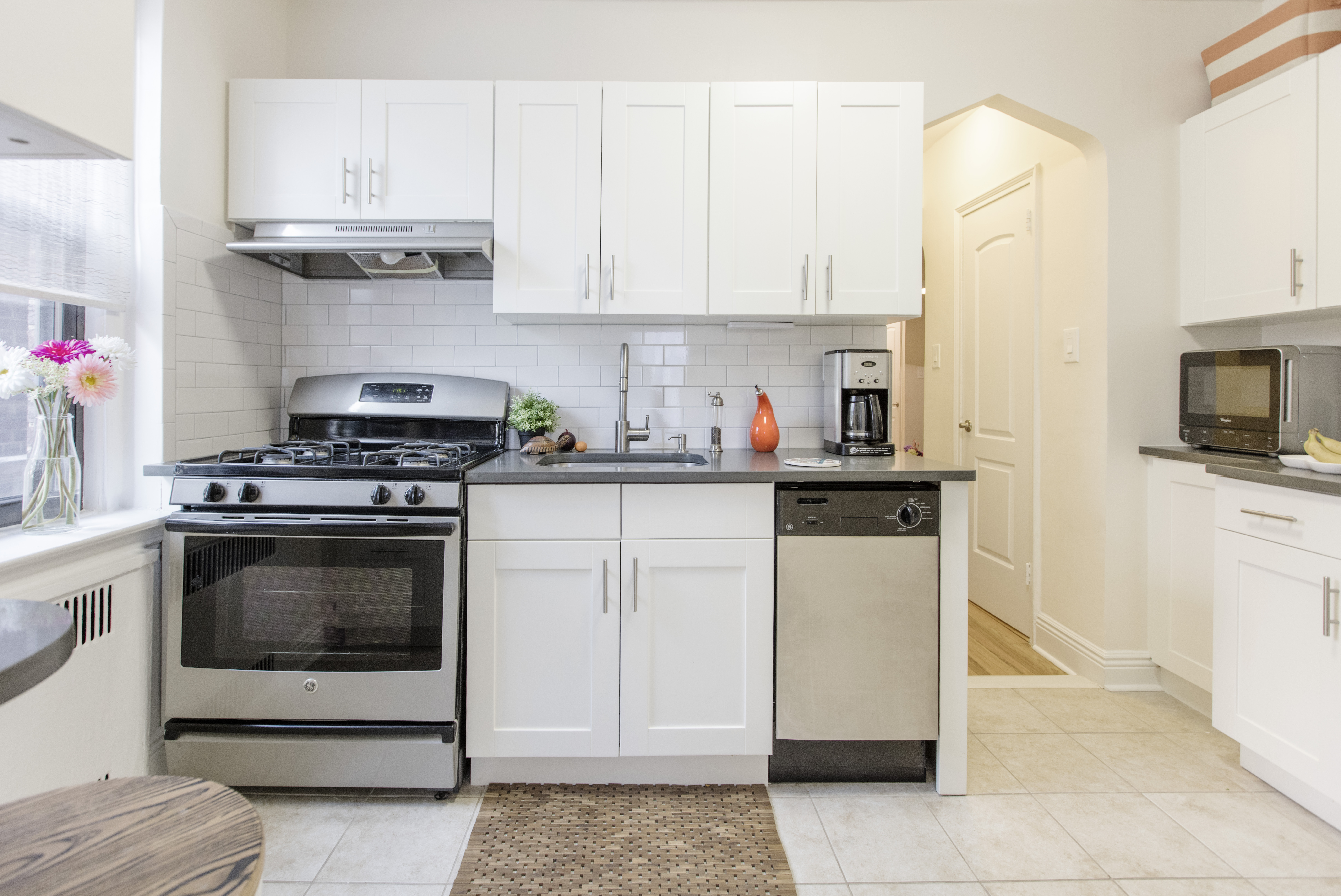 Bright modern kitchen with white shaker cabinets, stainless steel appliances, subway tile backsplash, and black countertops.