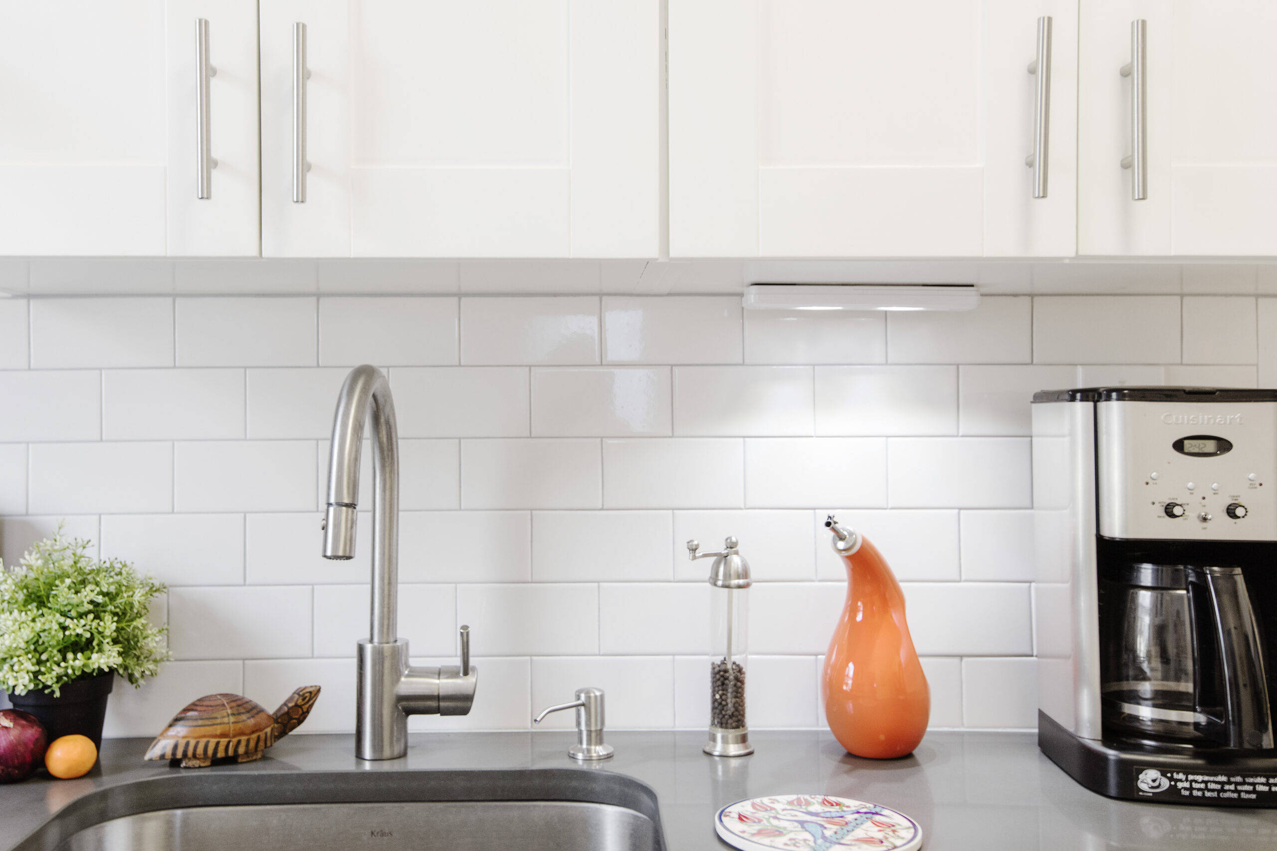 Close-up of a modern kitchen sink area with stainless steel faucet, white subway tile backsplash, and countertop accessories after a Ditmas Park apartment renovation.
