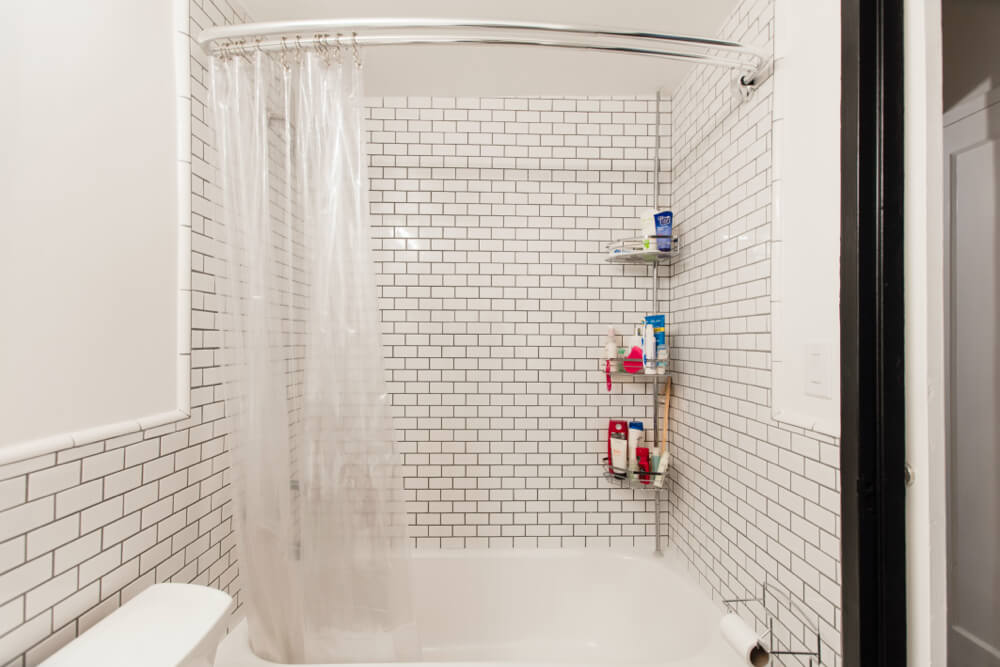 white bathroom with bathtub and subway tiles on walls and black door frame after renovation