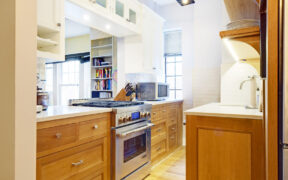 Custom millwork in a Manhattan kitchen with open oak drawers, glass-front cabinets, white counters, stainless range, bright lighting, and white oak flooring.