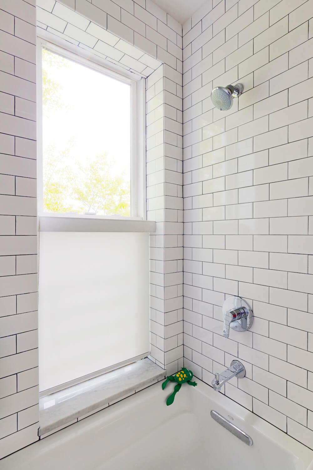 White bathroom with double hung window and white subway tiles over white bathtub after renovation
