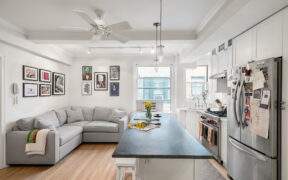 Hell’s Kitchen open kitchen and living area with a soapstone countertop island, white shaker cabinets, pendant lights, and bar seating for daily use.