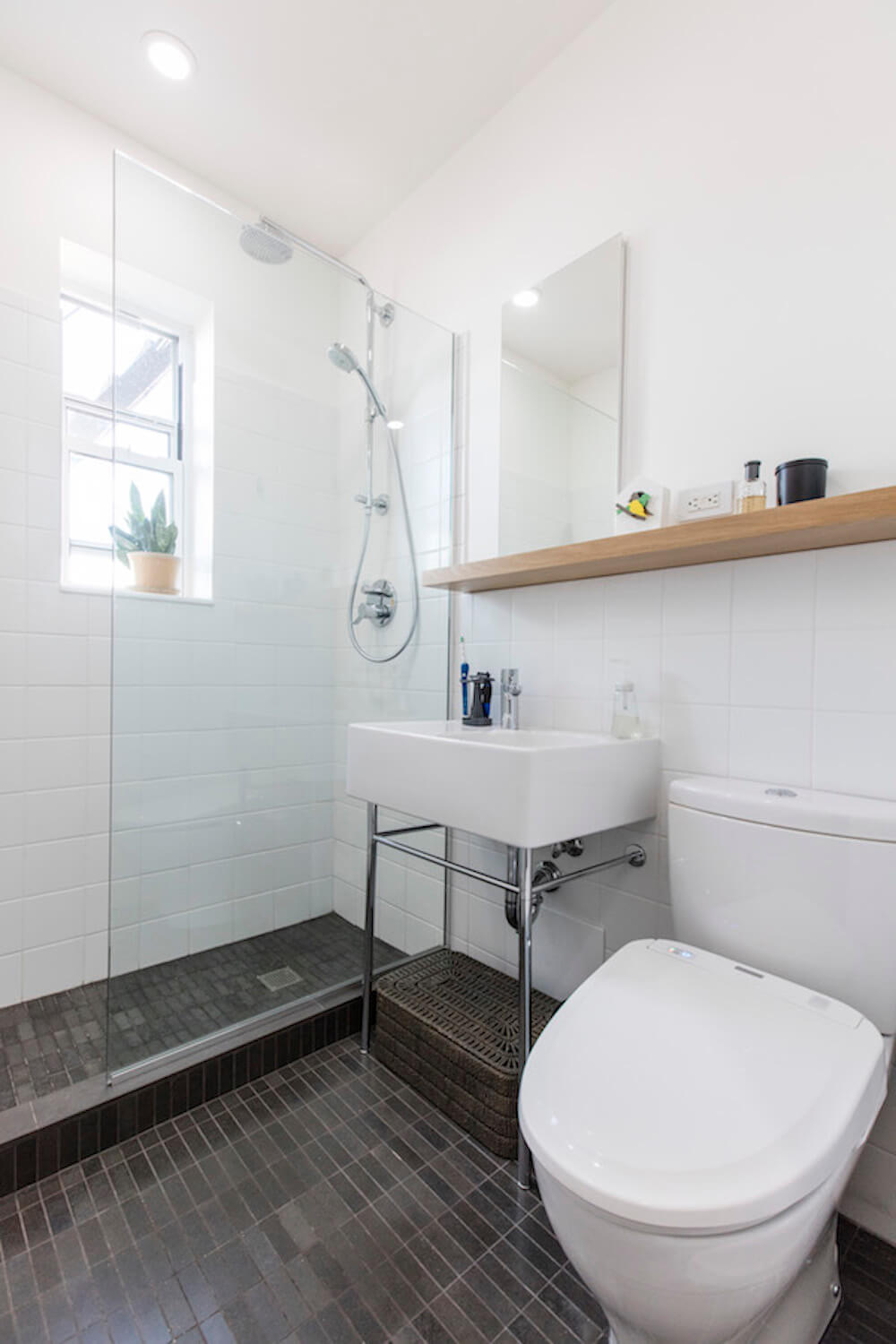 white bathroom with dark flooring and farmhouse sink on console legs and glass separator for walk in shower after renovation
