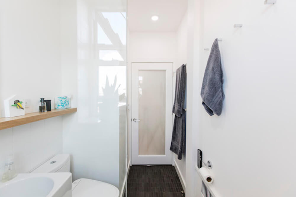 White bathroom with glass divider and white sink and towel hangers after renovation
