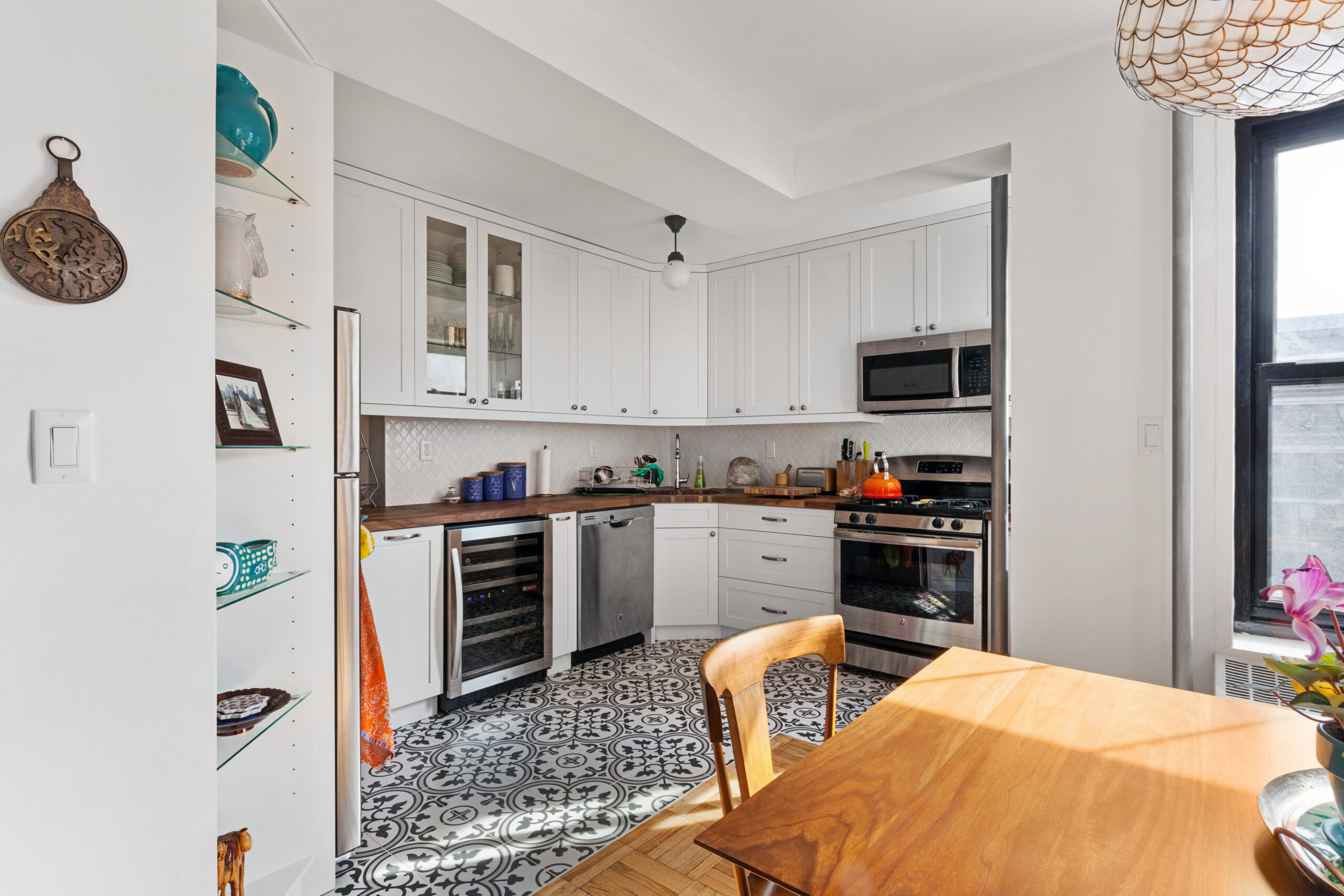A remodeled kitchen in Brooklyn showing patterned floor tile, walnut countertop, and white cabinets with wooden dining set