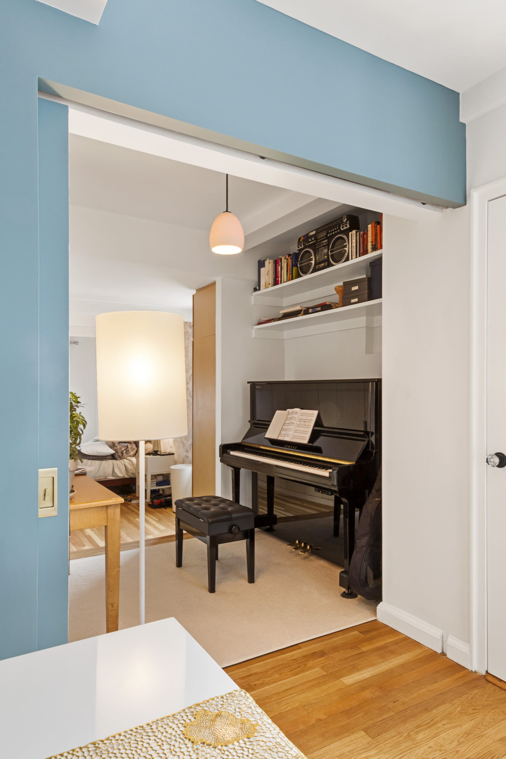 Chelsea piano nook after renovation with Hamilton Blue pocket door opening, upright piano, open shelves, refinished wood floors, and dining table nearby.