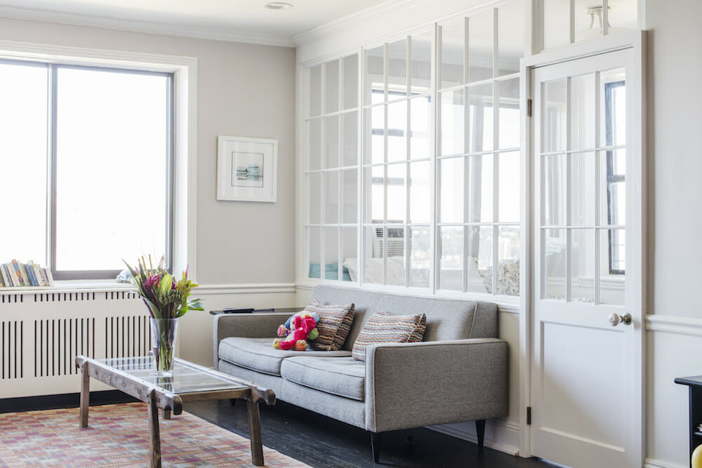 white glass panelled room divider in a white living room with large windows and gray couch after renovation