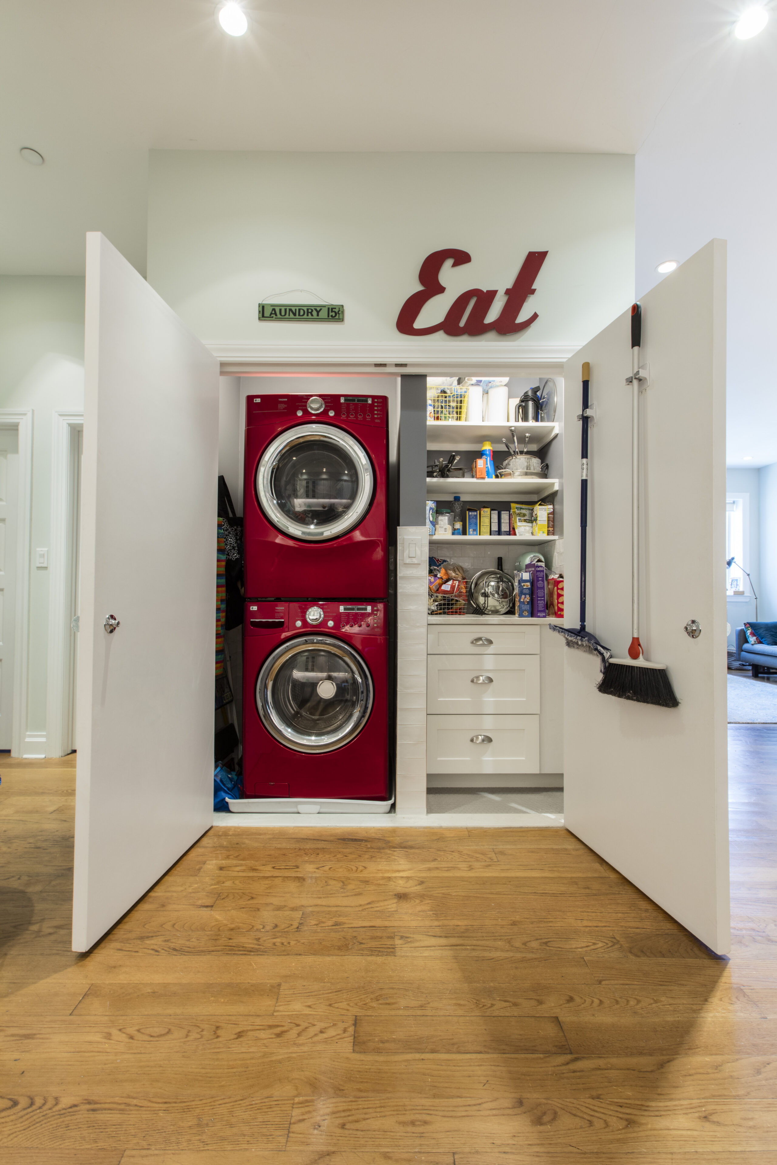 Brooklyn custom pantry and laundry closet with stacked red washer and dryer, open shelves, white drawers, broom storage, and wide double doors.