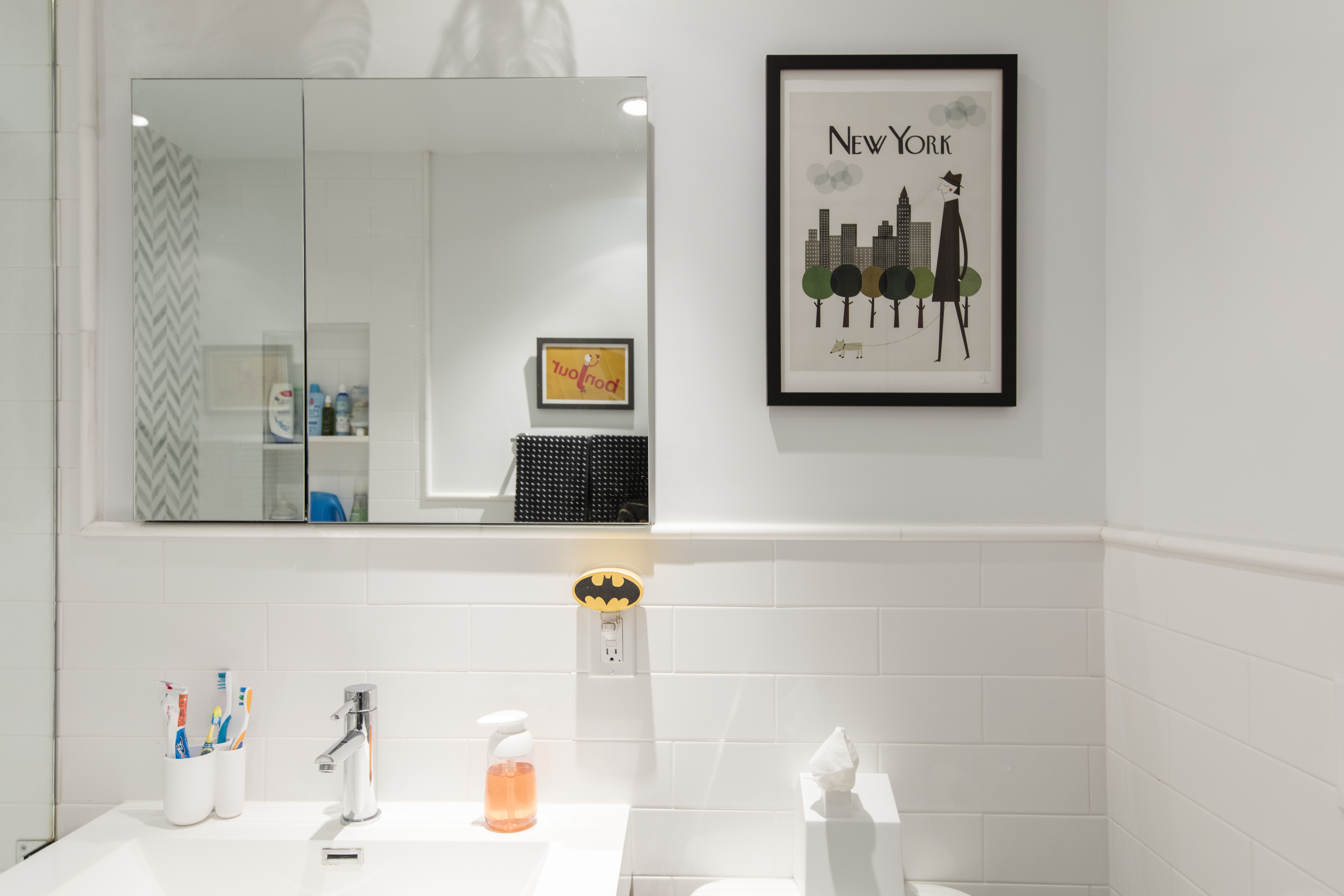 Brooklyn bathroom with white subway tile, floating vanity, wide mirrored cabinet, modern faucet, framed art, and bright recessed lighting.