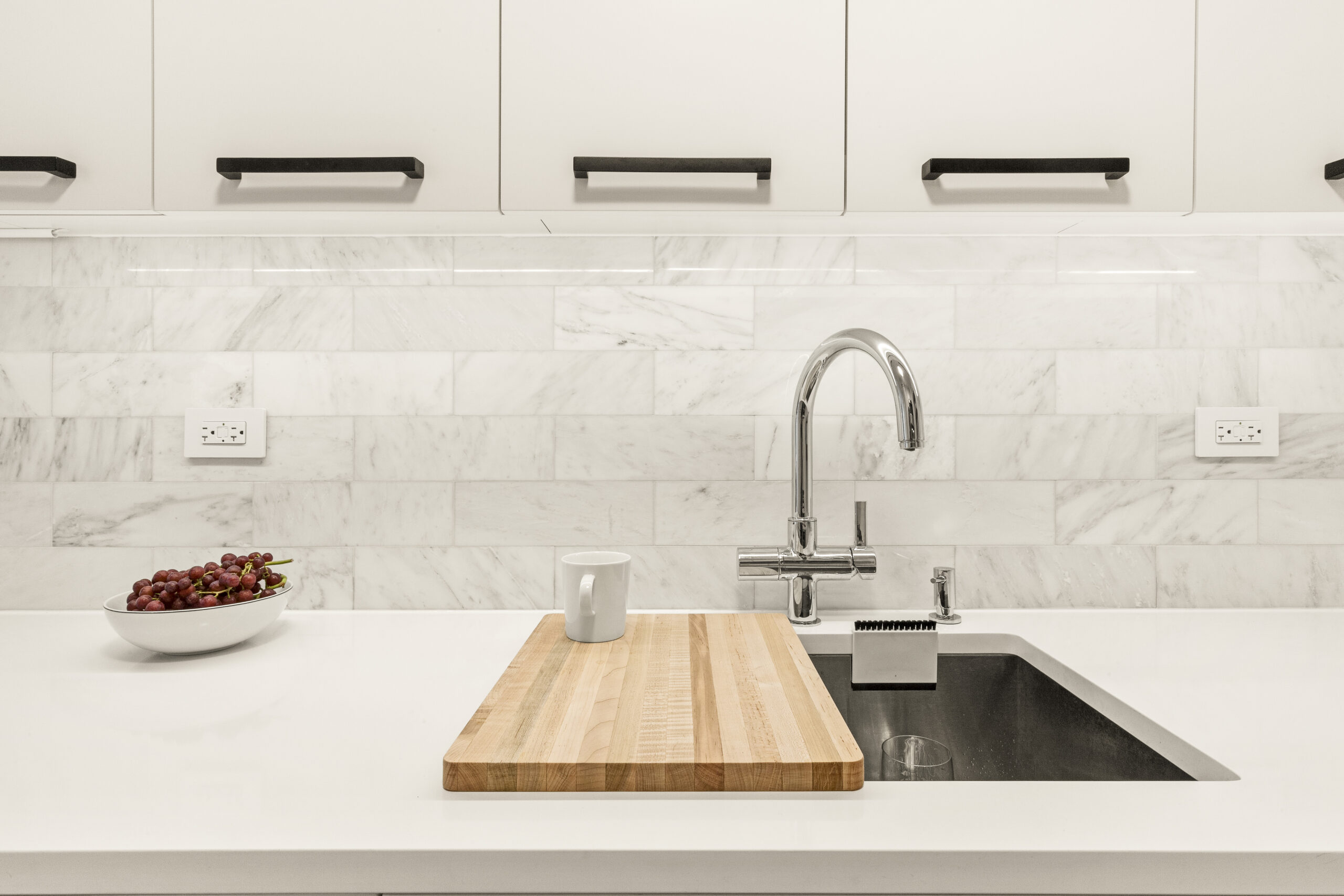 Tribeca kitchen detail after renovation with marble subway tile, white quartz counter, chrome faucet, undermount sink, and black cabinet pulls.