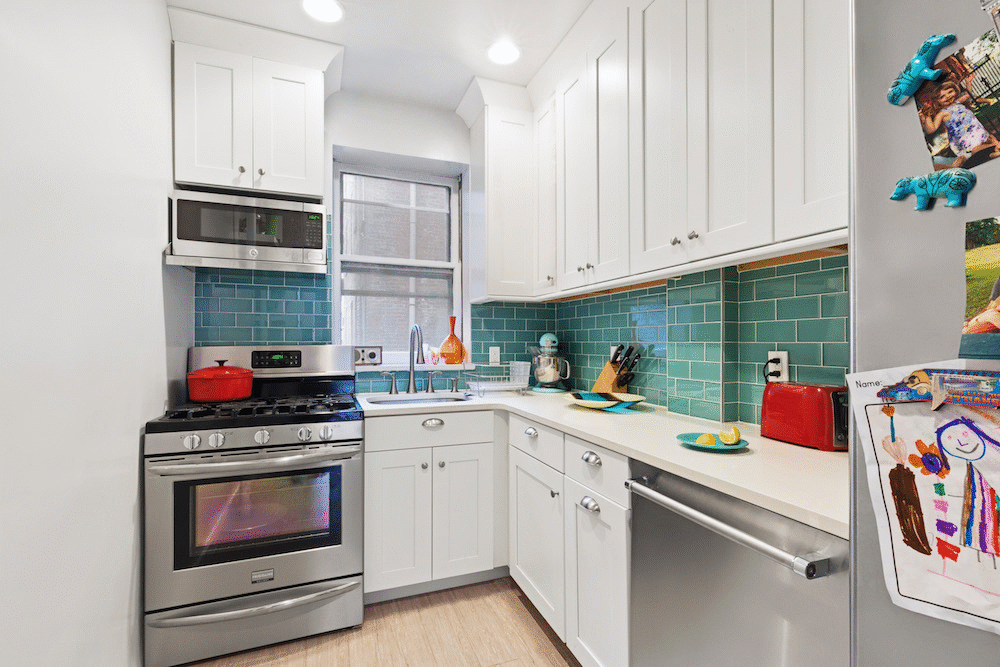 silver appliances in a small white kitchen with white cabinets and double hung window after renovation