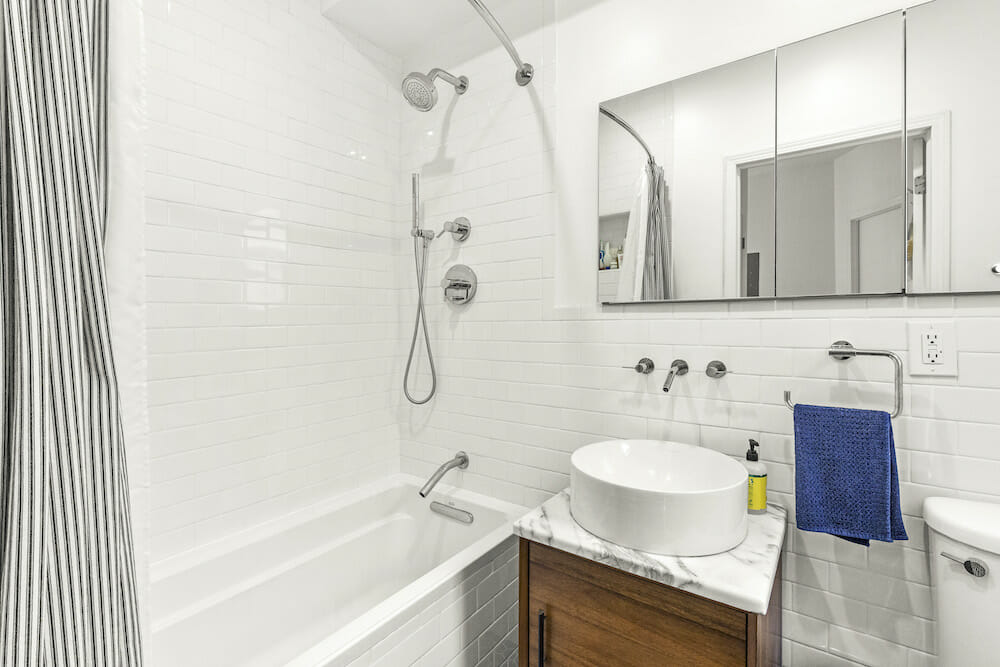 White bathroom with bathtub alongside sink and vanity below the bathroom mirrors after renovation 