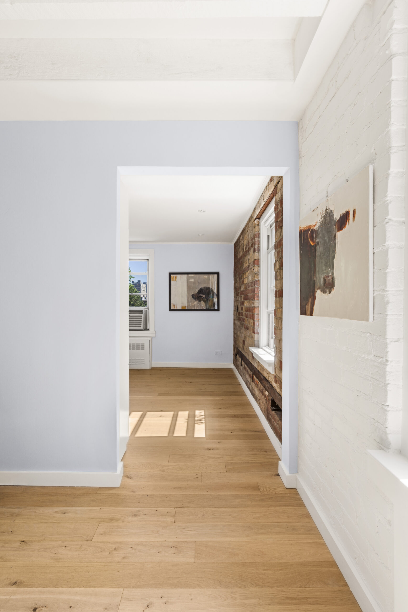 Cobble Hill co-op renovation showing a widened bedroom passage, white-painted brick, natural exposed brick, pale wood flooring, and crisp white trim.