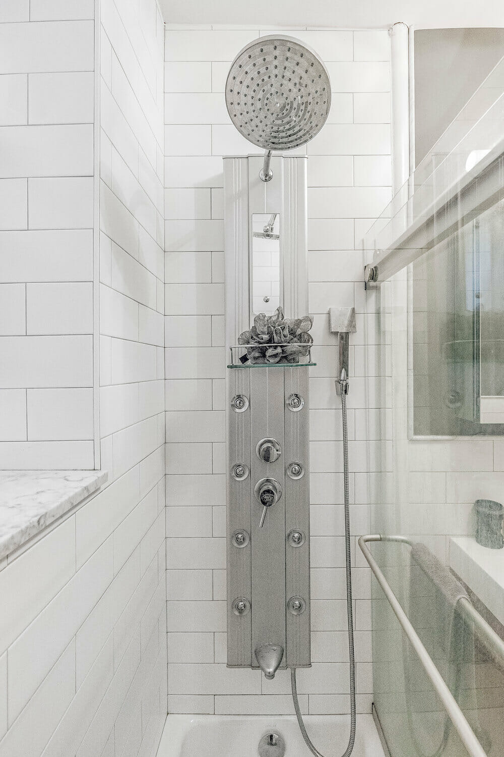 Narrow white shower area with nickel oversized shower head and bathroom fixtures after renovation