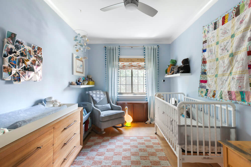 Blue nursery with white crib and baby quilt hanging on the wall after renovation