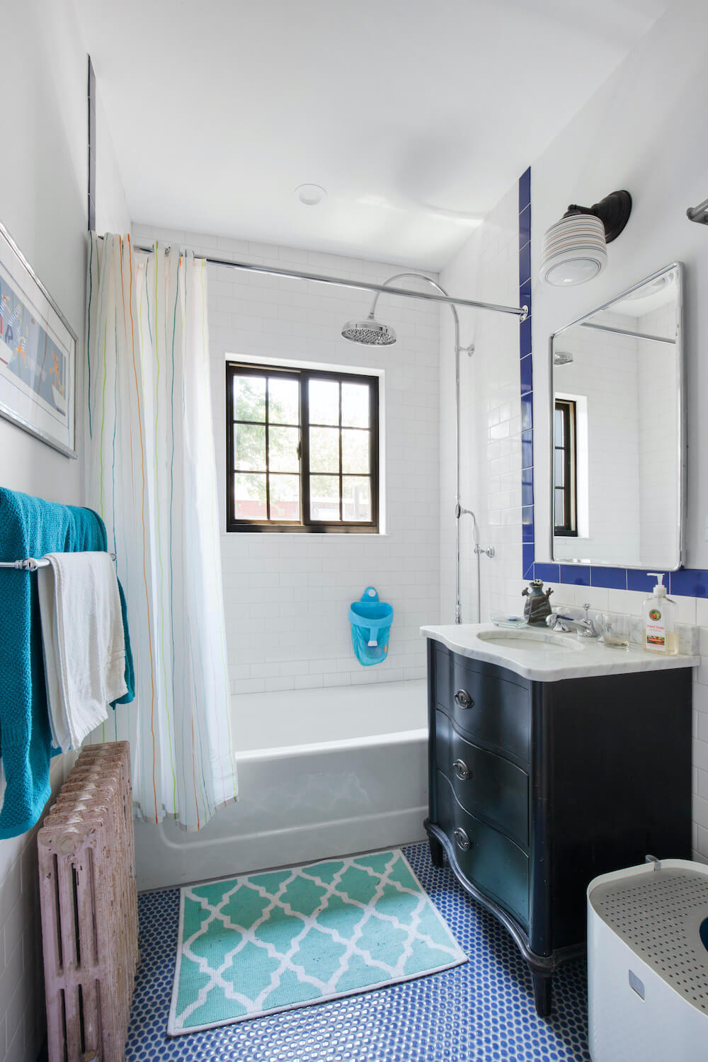 White bathtub in a white and blue bathroom with black vanity and oversized rainhead shower after renovation