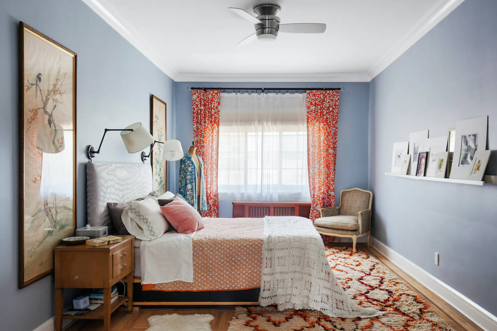 Blue bedroom with orange curtains on french window along with bed and headboard after renovation