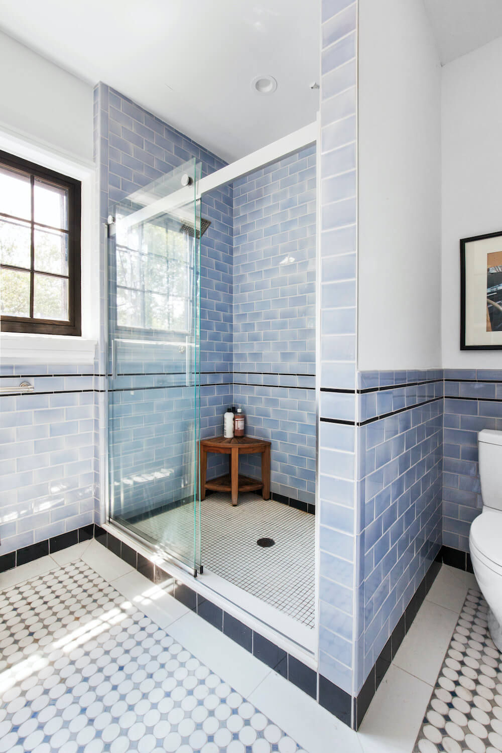 Shower area separated by glass doors in a white and blue bathroom with blue half tiles after renovation