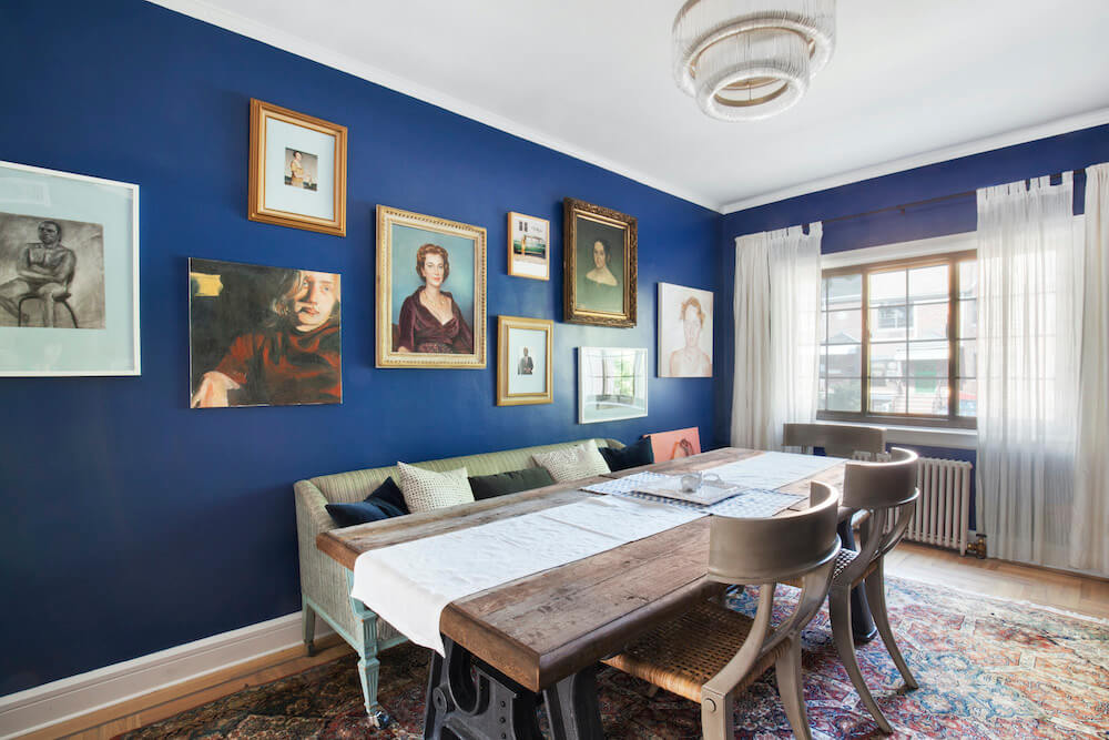 Blue dining space with paintings and white curtains after renovation
